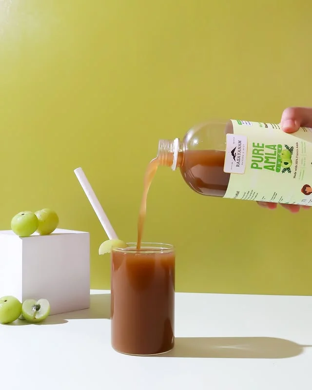 Pure Amla Juice poured from the bottle into a glass, on a yellow background.