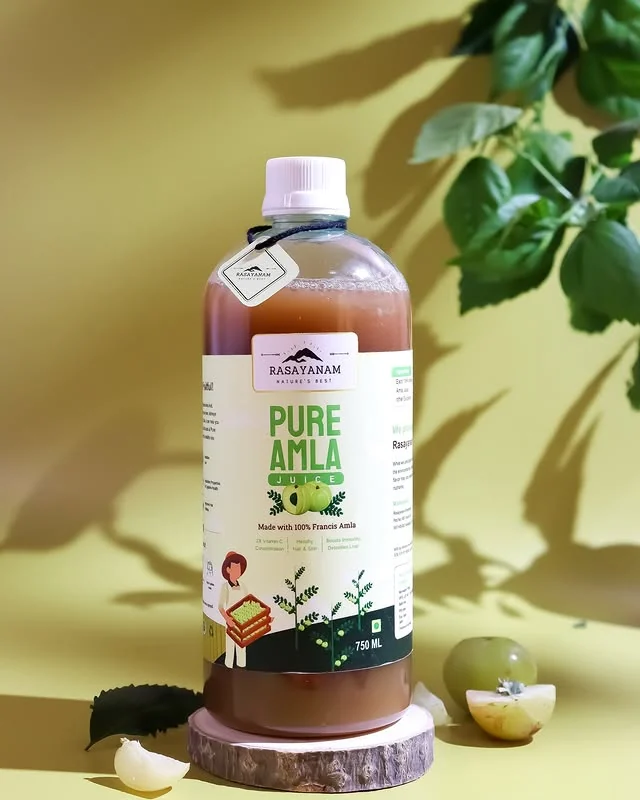 A bottle of Pure Amla Juice on a slice of wood, with leaves and amla fruit, on a yellow-green background.