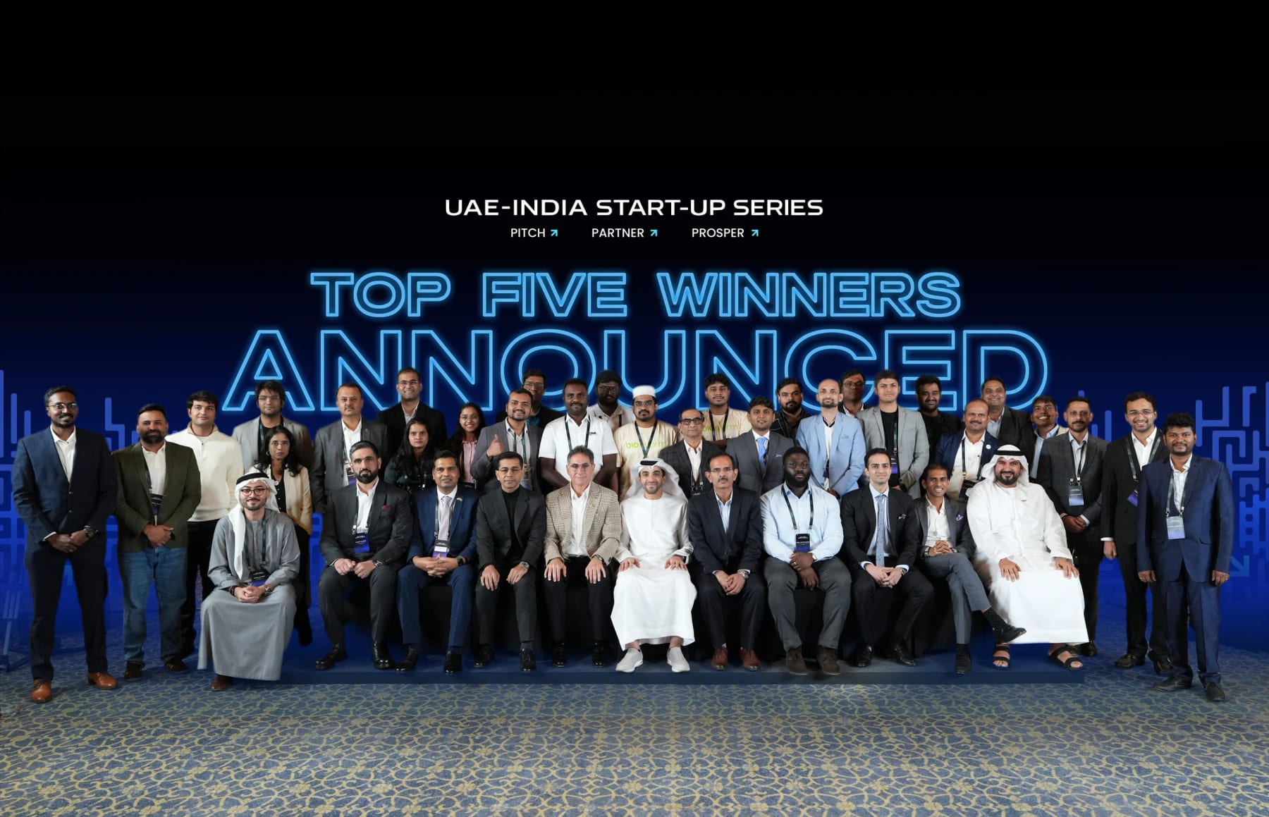 A group photo of participants and officials in front of a glowing backdrop reading “UAE–India Start-up Series — Top Five Winners Announced”.